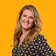 Smiling woman with blonde hair wearing a patterned blouse against an orange background.