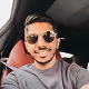 Smiling man wearing sunglasses and a gray shirt sitting in a car.