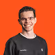 Smiling young man with short dark hair wearing a black sweatshirt against a bright orange background.