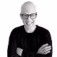 Smiling bald man wearing glasses and a black shirt, posing with arms crossed against a white background.