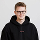 Young man wearing glasses and a black hoodie smiling against a light gray background.