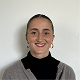 Smiling woman with dark hair pulled back, wearing a gray cardigan over a black turtleneck against a plain white background.